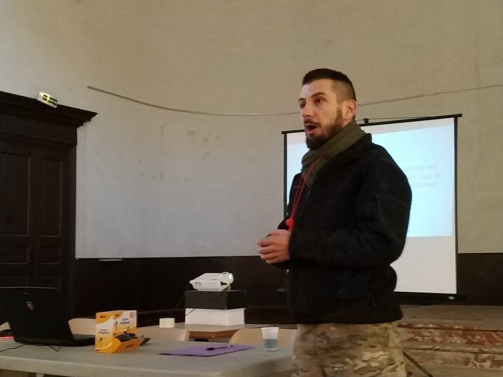 Dereck CARRILLO donnant une présentation sur la gestion de crise, avec un projecteur et un ordinateur portable sur une table, dans un environnement intérieur.